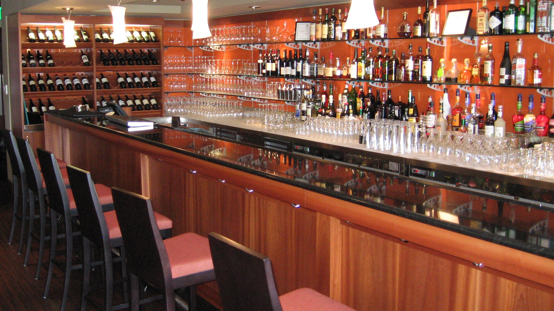 Finished Port O' Call with black and red high chairs, wood front bar with smooth glossy bar top, liquor bottles shown behind
